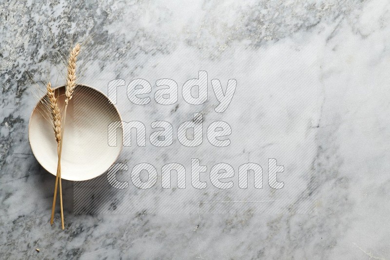 Wheat stalks on Beige Pottery Plate on grey marble flooring, Top view