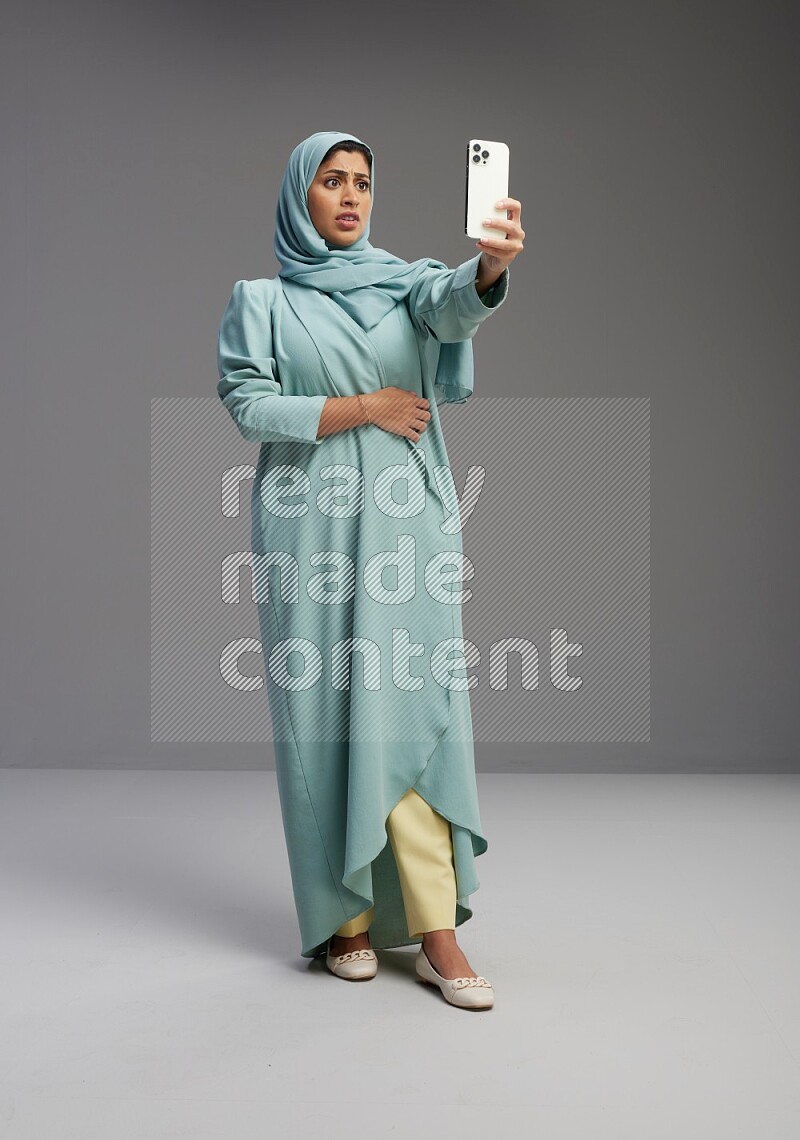 Saudi Woman wearing Abaya standing taking selfie on Gray background