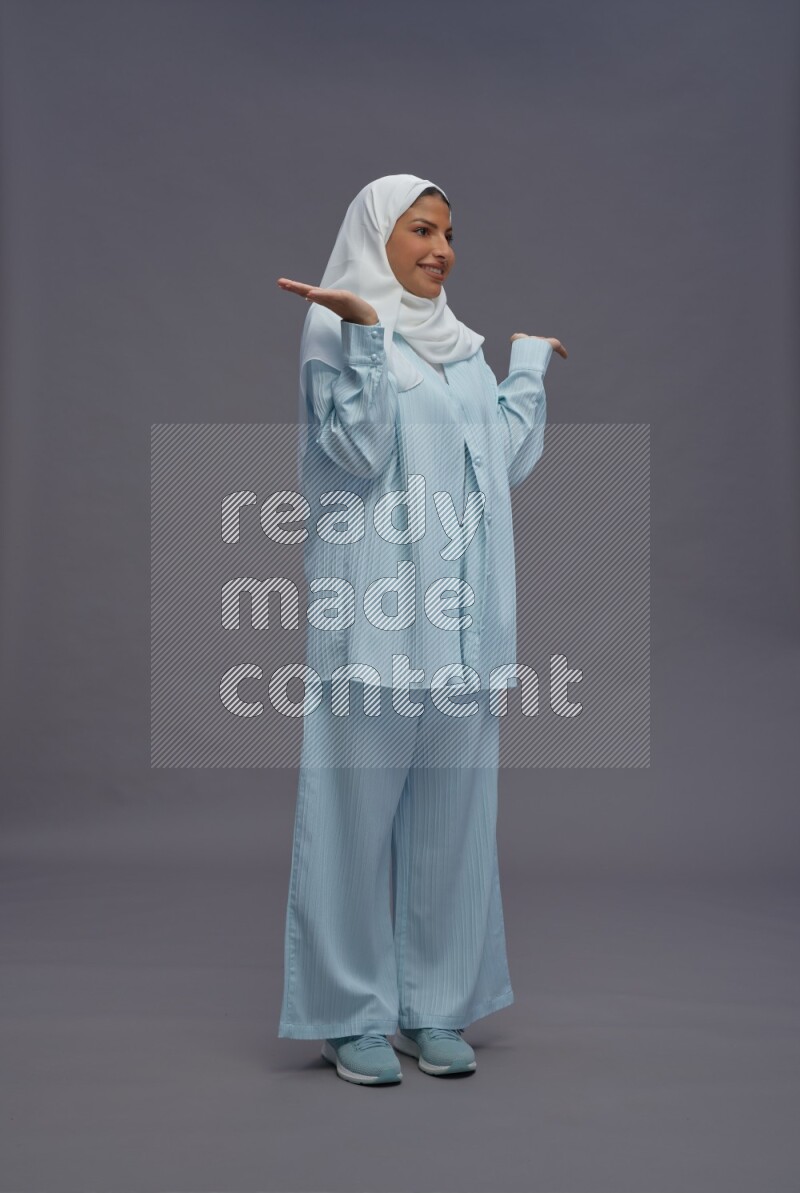 Saudi woman wearing hijab clothes standing interacting with the camera on gray background