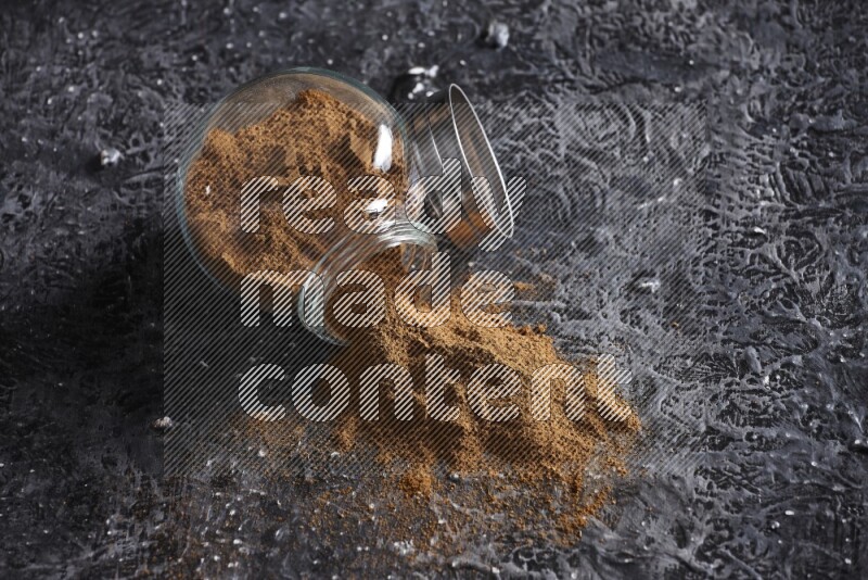 Flipped herbal glass jar full of cinnamon powder on textured black background