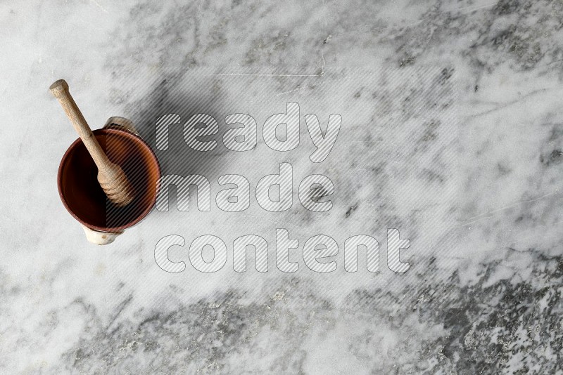 Decorative Pottery Pot with wooden honey handle in it, on grey marble flooring, Top View