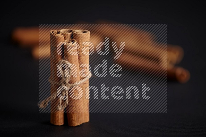 4 Cinnamon sticks stacked and bounded with more sticks in the background on black flooring