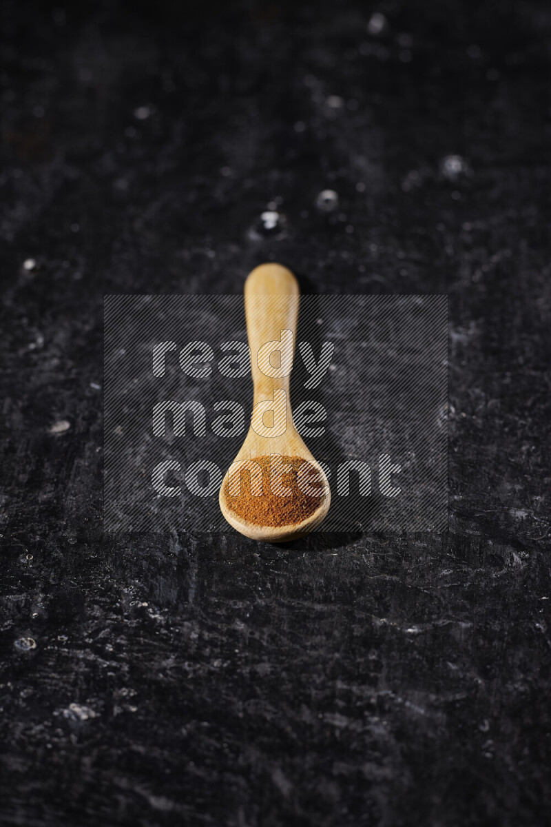 A wooden spoon full of ground paprika powder on black background