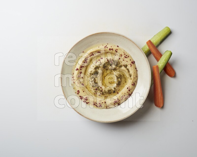 Hummus in a pottry plate garnished with zaatr & sumak on a white background