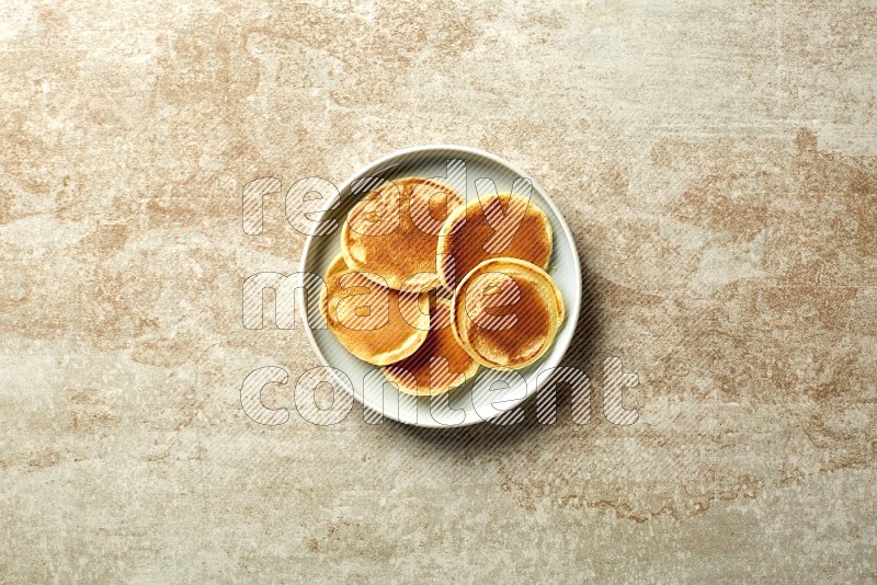 Five stacked plain mini pancakes in a blue plate on beige background