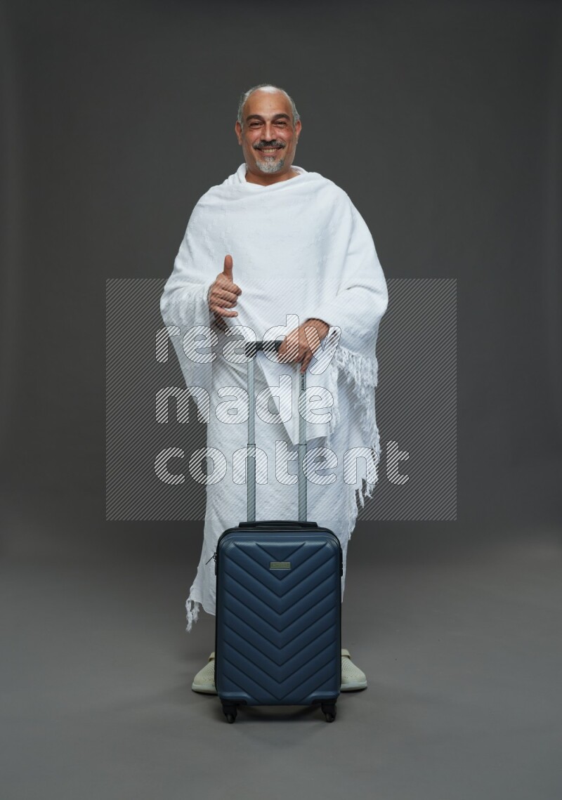 A man wearing Ehram Standing holding traveling bag on gray background