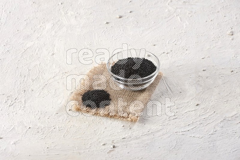 A glass bowl full of black seeds set on a burlap piece on textured white flooring in different angles