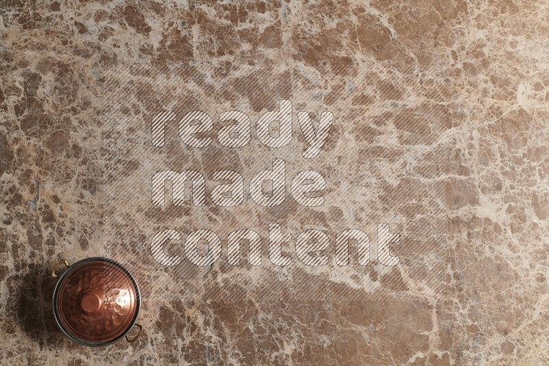 A small copper pot on beige marble background