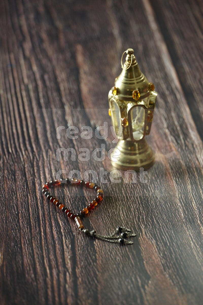 A golden lantern with different drinks, dates, nuts, prayer beads and quran on brown wooden background