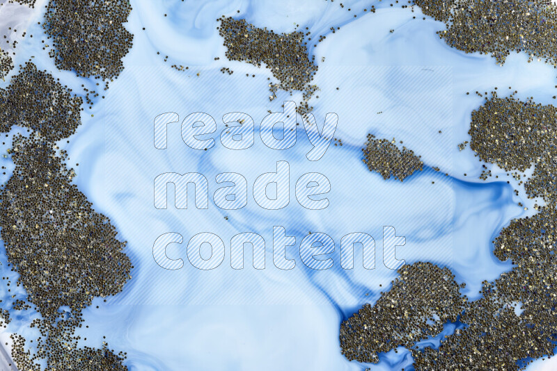 A close-up of sparkling gold glitter scattered on swirling blue background