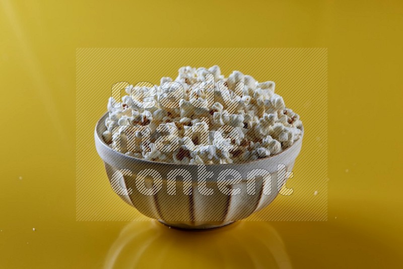 A white pottery bowl full of popcorn on a yellow background in different angles