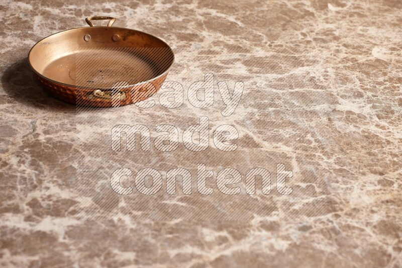 A small copper pan on beige marble background