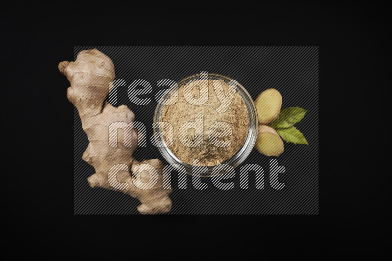 A glass bowl full of ground ginger powder on black background