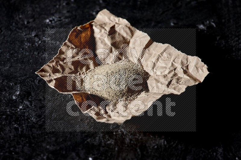 White pepper powder in a crumpled paper on textured black flooring