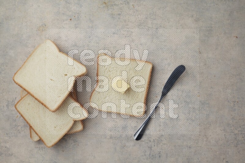 White toast slices with a butter cube and a spreading knife on a light blue textured background