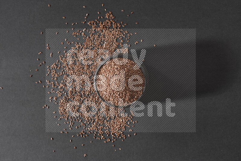 وعاء فخاري أسود ممتلئ بحبوب بذر الكتان محاط بالبذور على أرضية سوداء