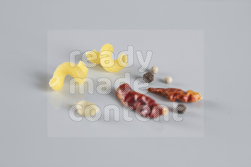 Raw pasta with different ingredients such as cherry tomatoes, garlic, onions, red chilis, black pepper, white pepper, bay laurel leaves, rosemary, cardamom and mushrooms on light blue background