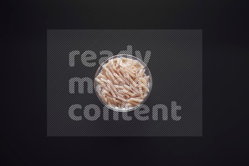 Mini penne pasta in a glass bowl on black background