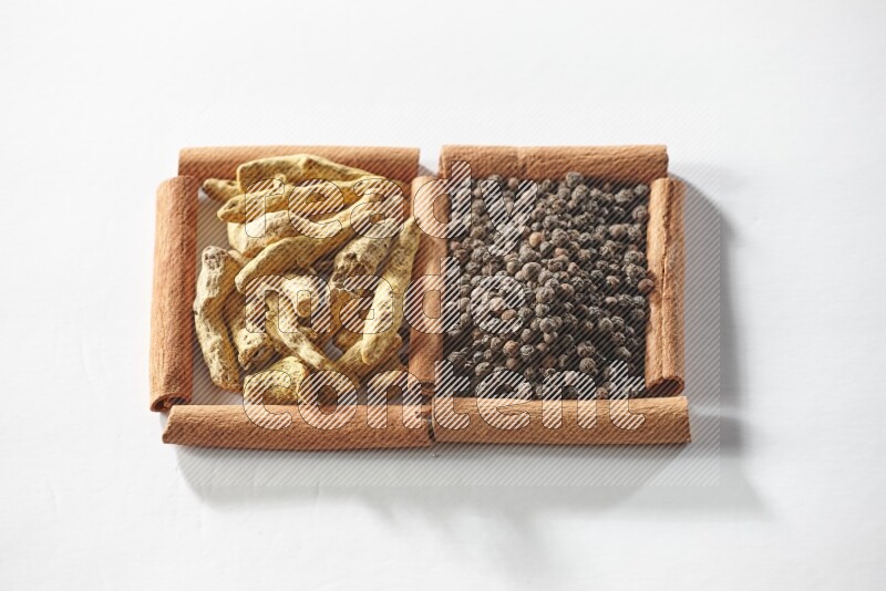 2 squares of cinnamon sticks full of black peppers and turmeric fingers on white flooring
