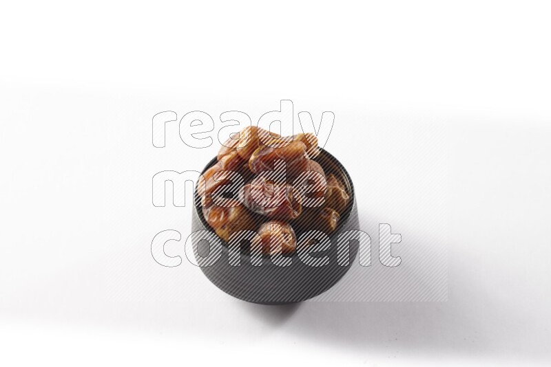 Dates in a black pottery bowl on white background