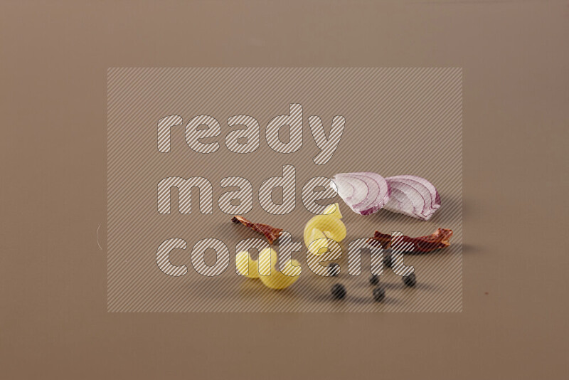 Raw pasta with different ingredients such as cherry tomatoes, garlic, onions, red chilis, black pepper, white pepper, bay laurel leaves, rosemary and cardamom on beige background