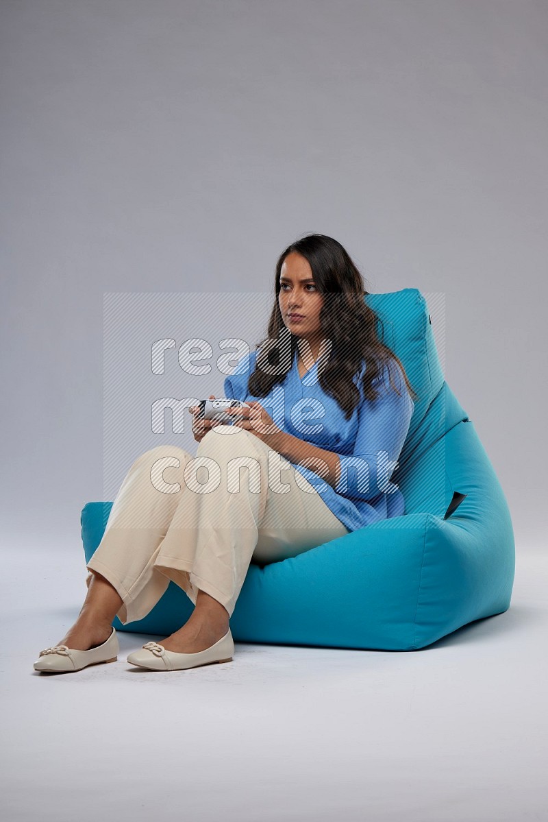 A woman sitting on a blue beanbag and gaming with joystick