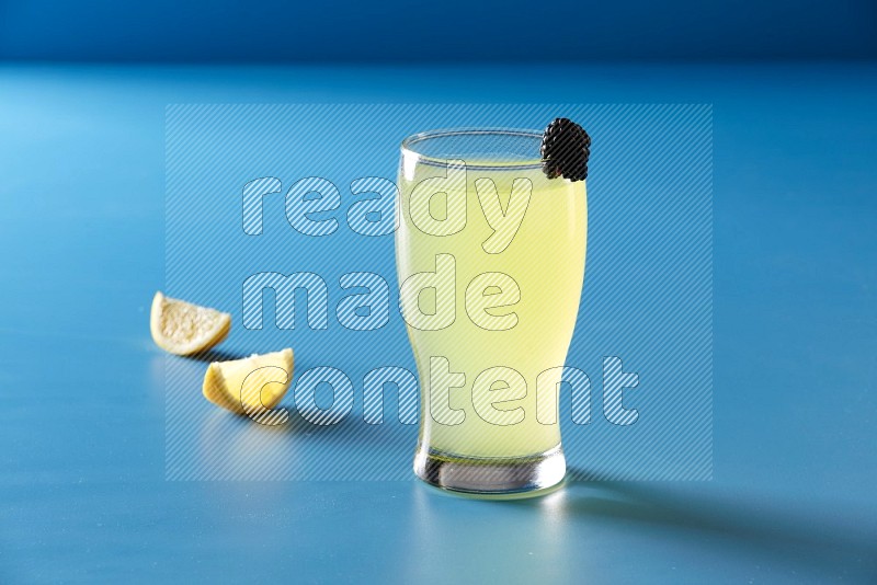 glass of lemon juice with berry on blue background