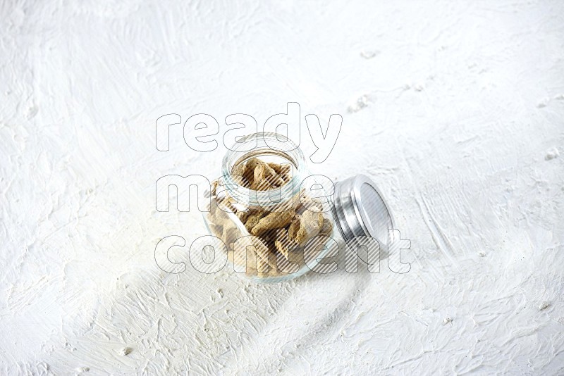 A glass spice jar full of dried turmeric whole fingers on a textured white flooring