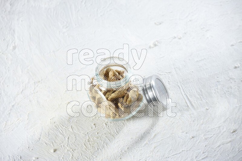 A glass spice jar full of dried turmeric whole fingers on a textured white flooring