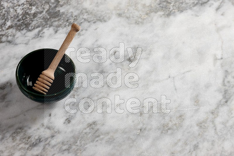 Dark green Pottery Bowl with wooden honey handle in it, on grey marble flooring, 65 degree angle