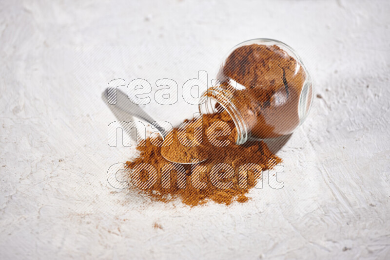 A glass jar full of ground paprika powder flipped with some spilling powder on white background