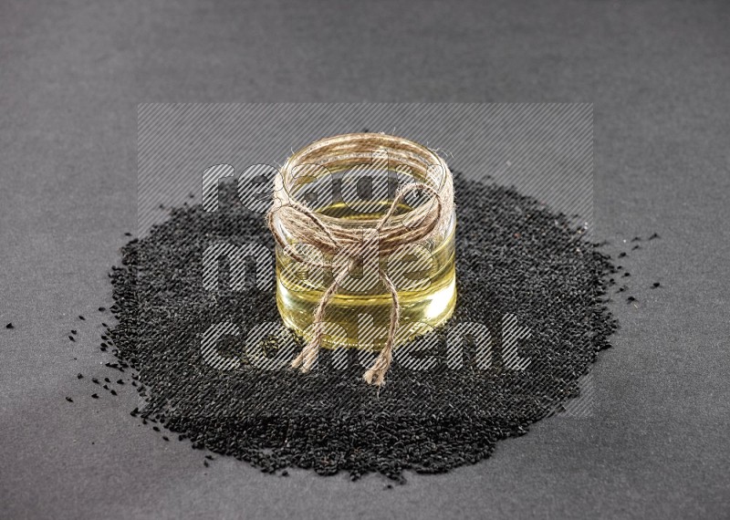 A glass jar full of black seeds oil surrounded by the seeds on a black flooring in different angles