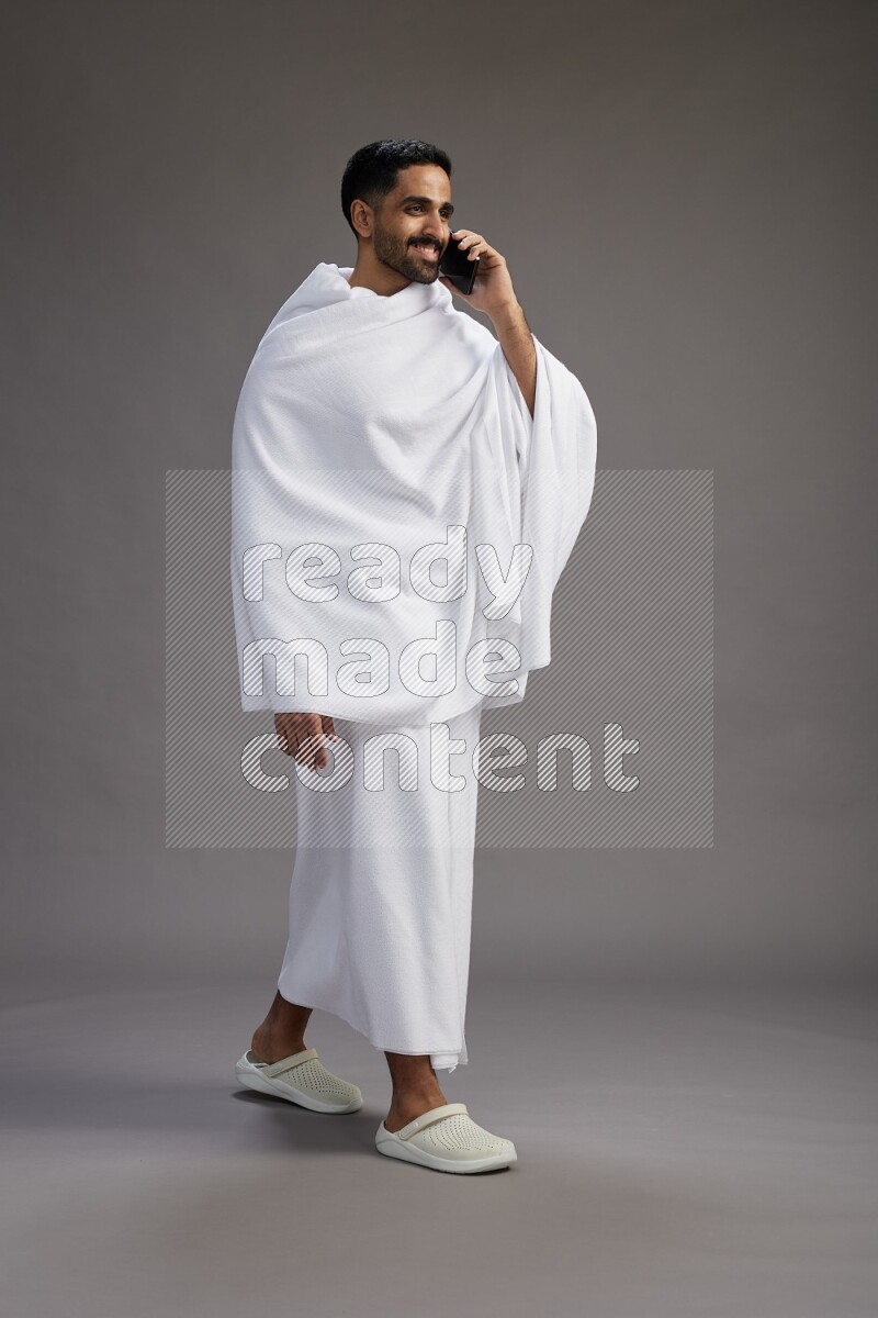 A man wearing Ehram Standing talking on phone on gray background