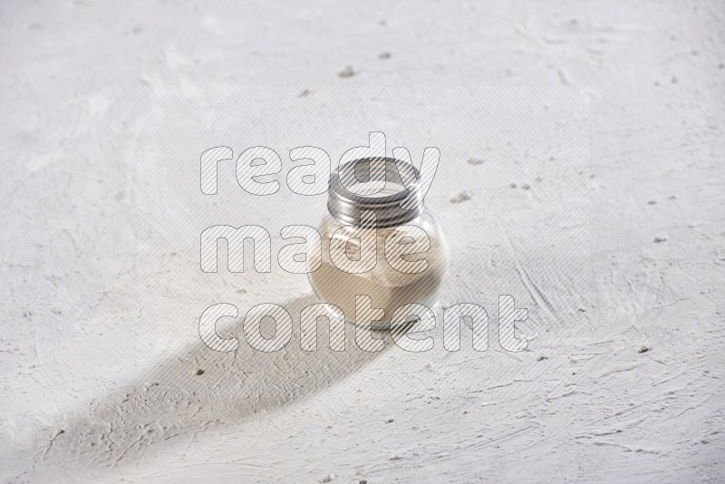 A glass spice jar full of garlic powder on a textured white flooring