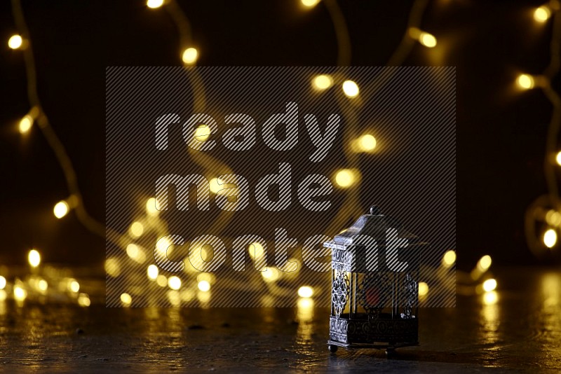 A silver lantern with fairy light in a dark setup