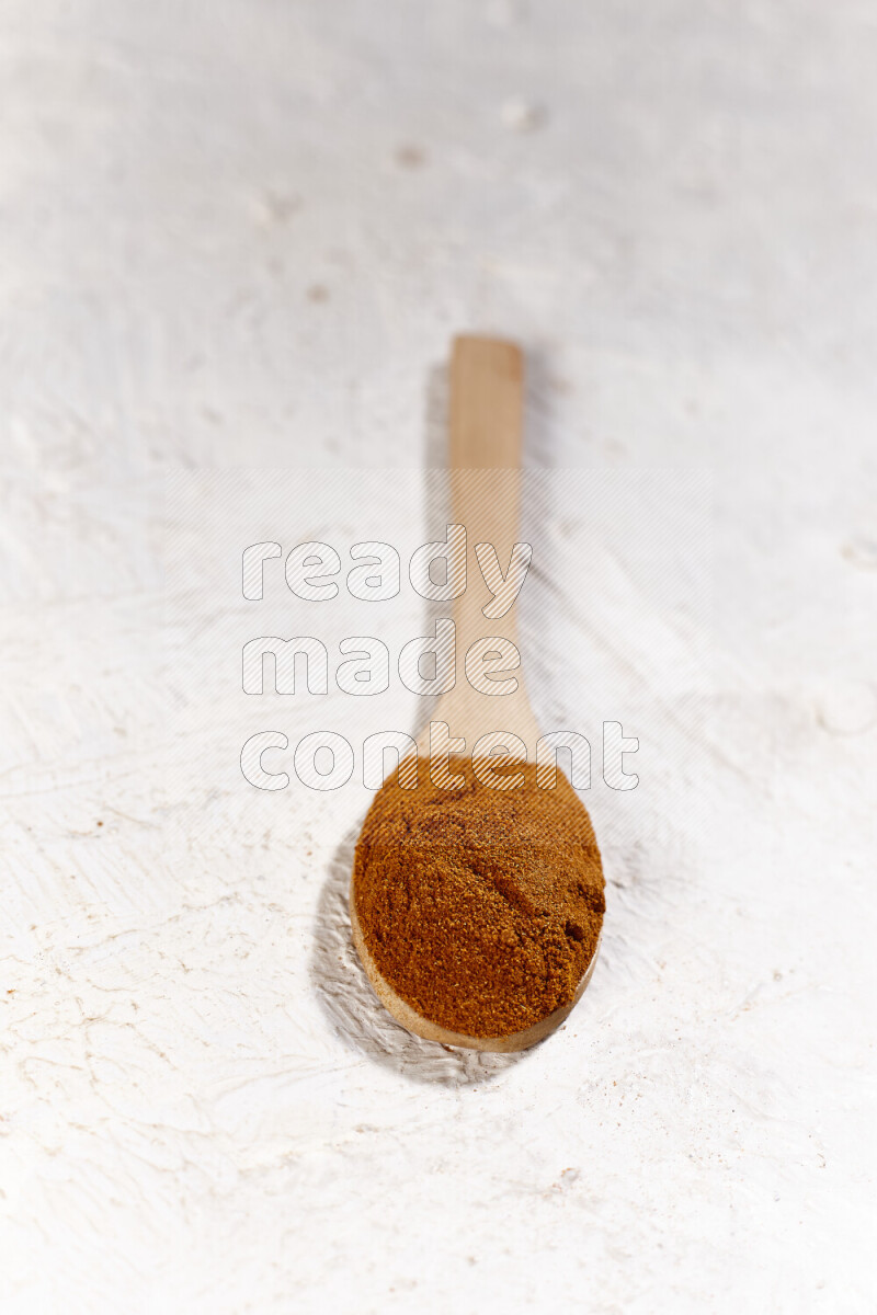 A wooden spoon full of ground paprika powder on white background