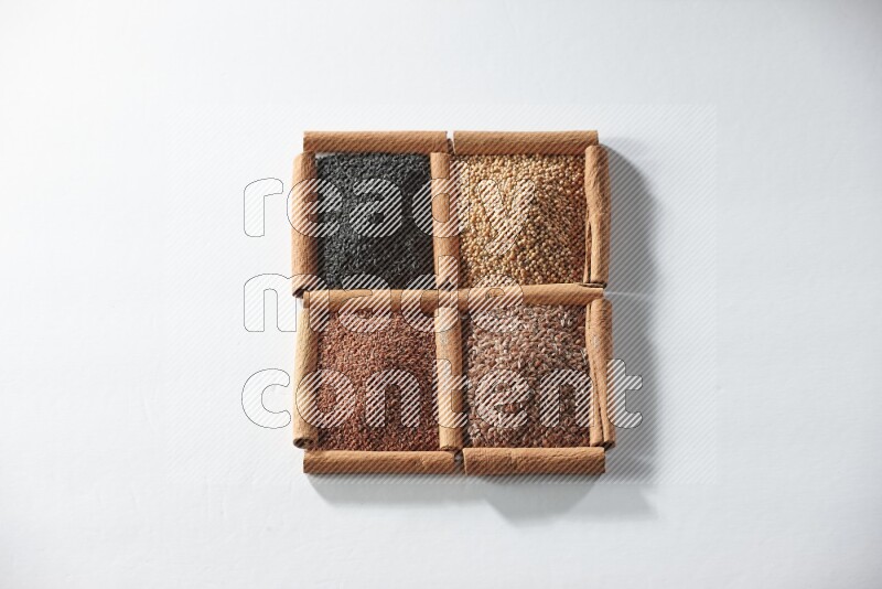 4 مربعات من أعواد القرفة ممتلئة بحبة البركة وبذور الخردل وبذور الكتان وحب الرشاد على أرضية بيضاء