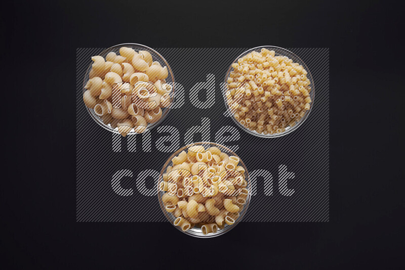 Different pasta types in glass bowls on black background