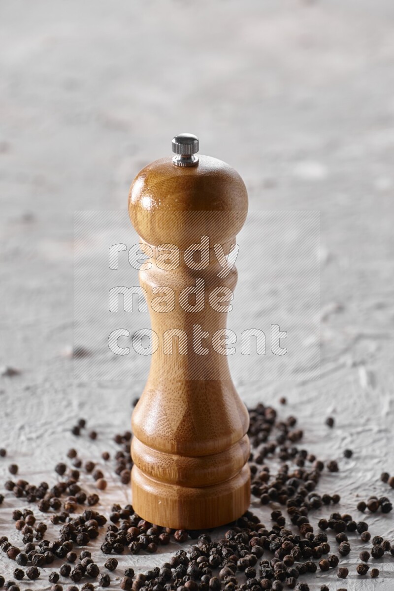A wooden grinder with black pepper beads on a textured white flooring