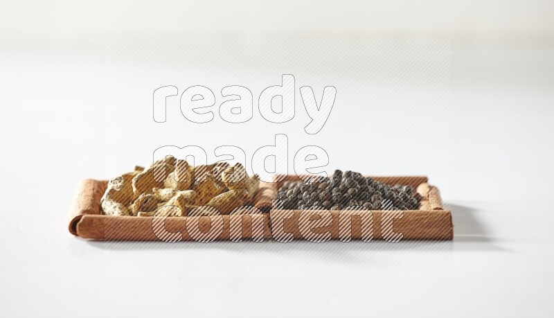 2 squares of cinnamon sticks full of black peppers and turmeric fingers on white flooring