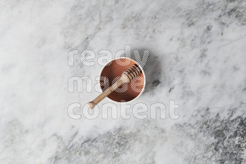 Multicolored Pottery bowl with wooden honey handle in it, on grey marble flooring, Top View