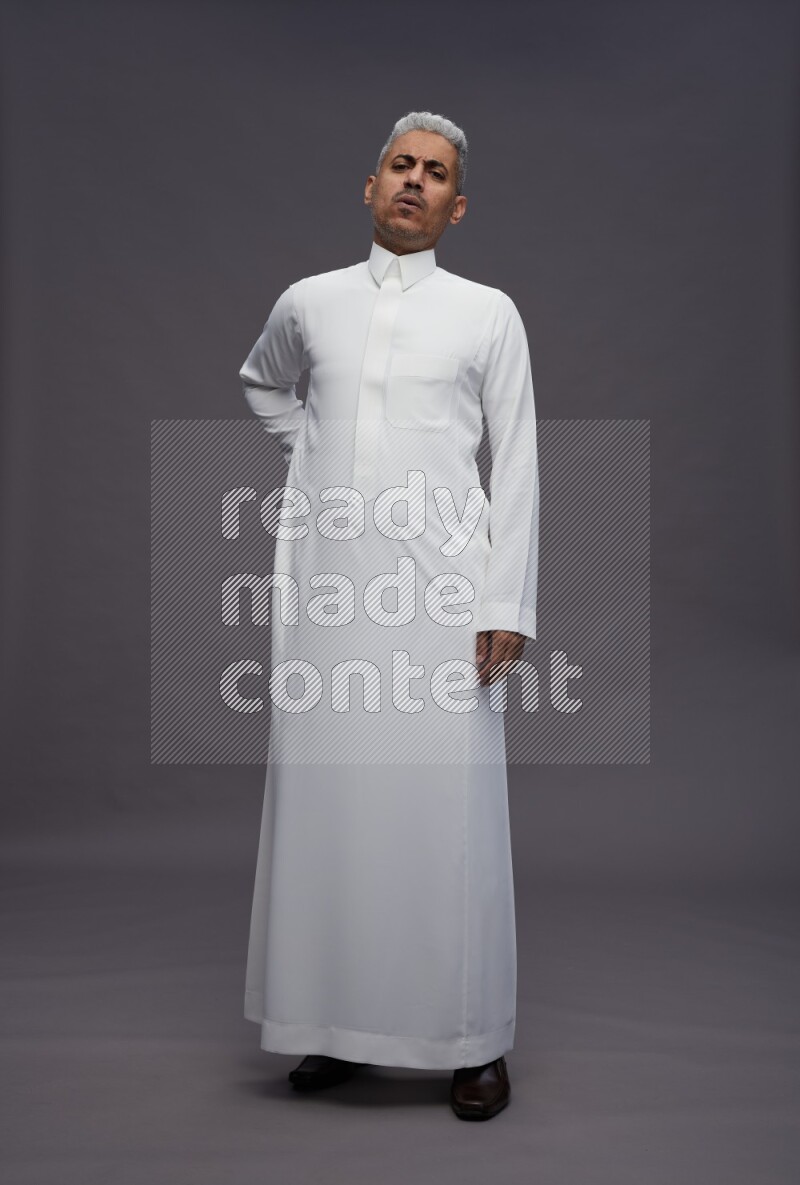 Saudi man wearing thob standing interacting with the camera on gray background