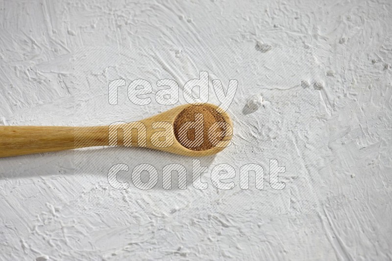 Cinnamon powder in a wooden spoon on a white background