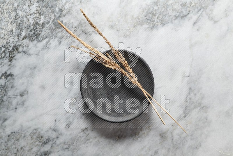 Wheat stalks on Black Pottery Plate on grey marble flooring, Top view