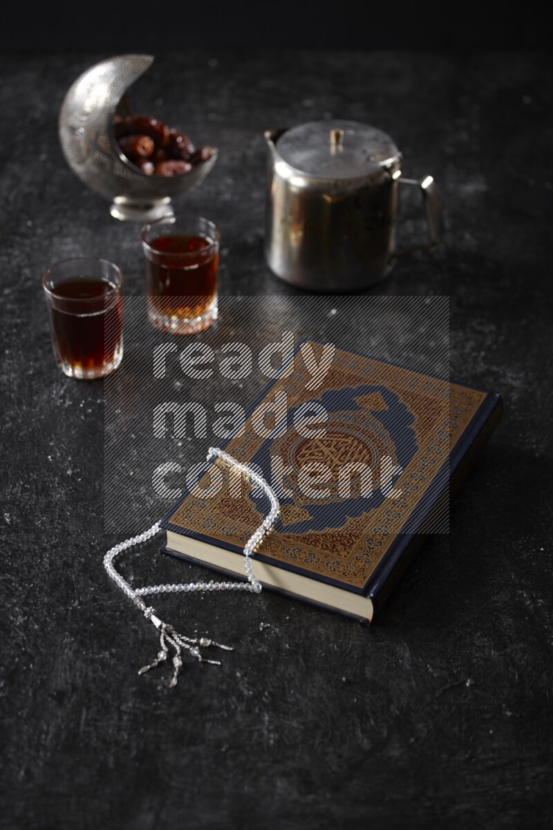 مصحف مع فناجين شاي وسبحة علي خلفية سوداء خشبية