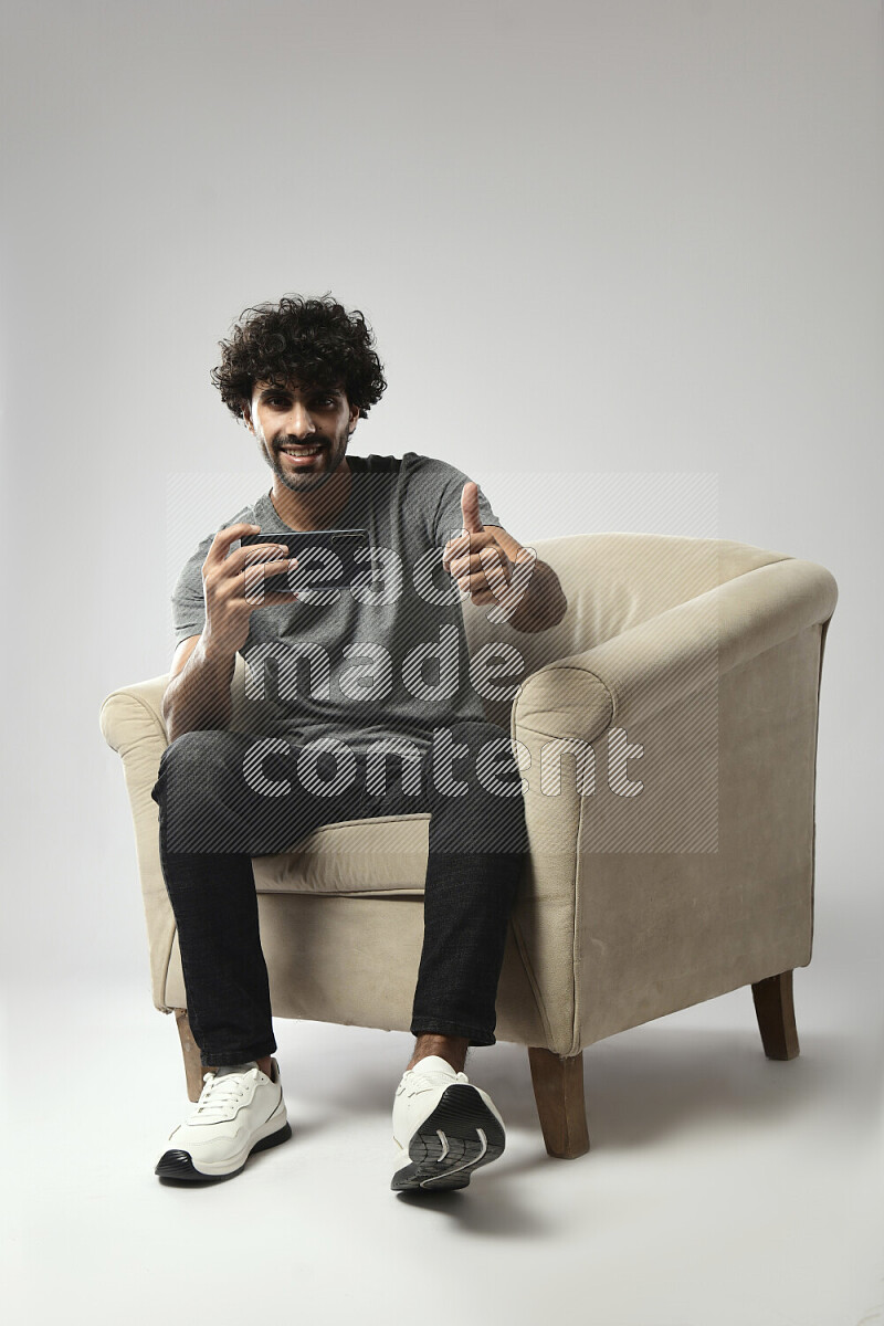 A man wearing casual sitting on a chair shooting with his phone on white background