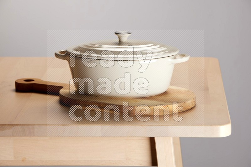white ceramic pot on an oval  wooden cutting board on the edge of wooden table