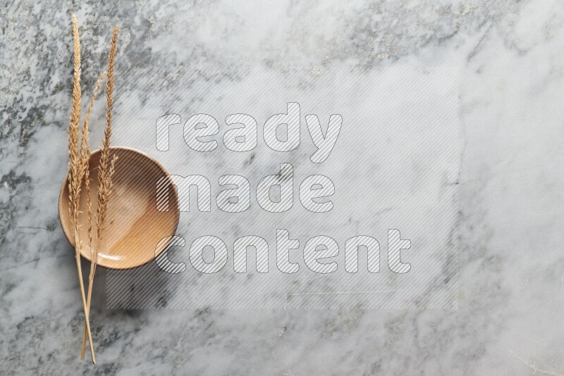 Wheat stalks on multicolored pottery plate on grey marble background