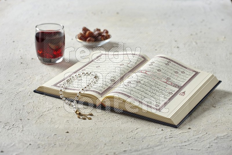 Quran with dates, prayer beads and different drinks all placed on textured white background