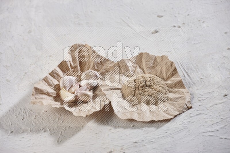 2 crumpled piece of paper full of garlic cloves and powder on a textured white flooring
